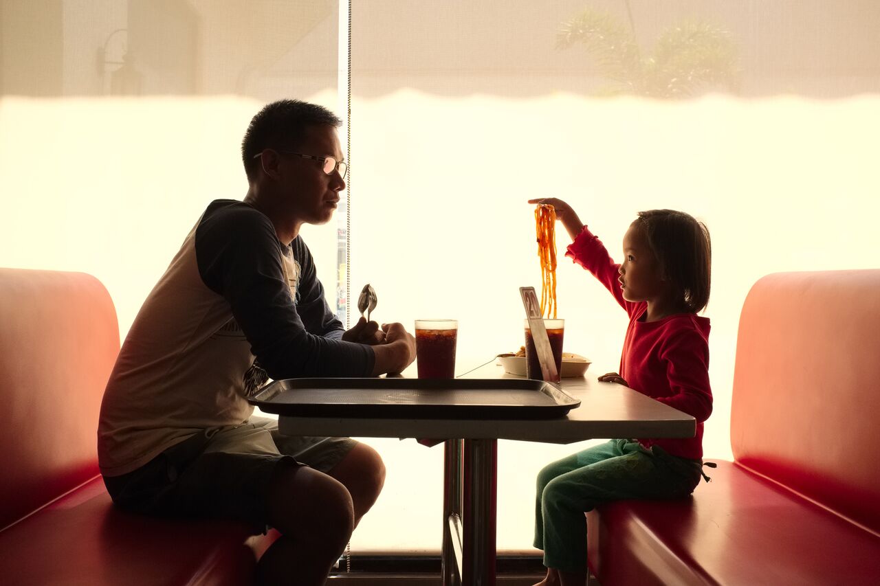 Dennis and his daughter Dennis-Ann eat lunch at the local Jollybee fast food restaurant in Tarlac, Philippines. Since Dennis-Ann's mother Glory Ann went to work as a domestic worker in Hong Kong, Dennis has looked after his daughter. 