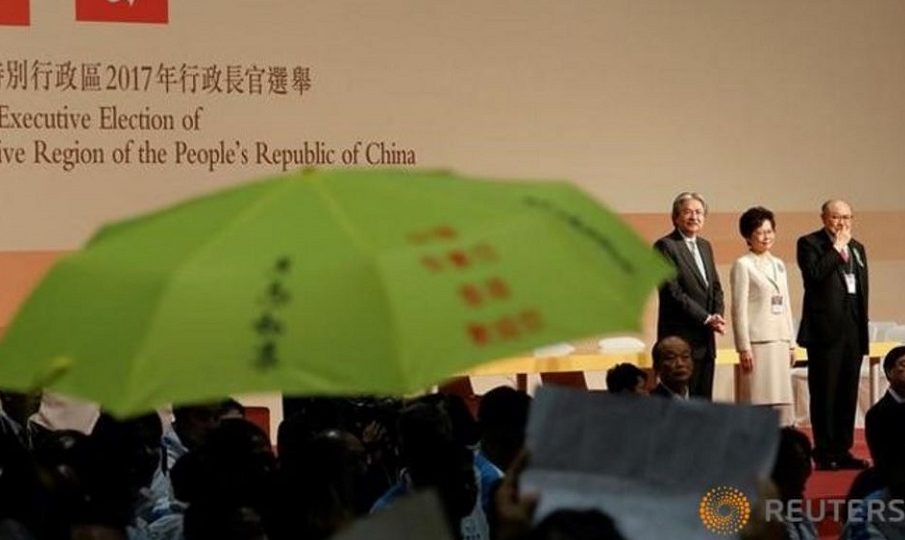 A yellow umbrella, the symbol of the Occupy Central movement, is displayed before candidates John Tsang, Carrie Lam and Woo Kwok-hing (L-R) as Lam is announced the winner of the election for Hong Kong’s Chief Executive in Hong Kong, March 26, 2017. Photo: Tyrone Siu/Reuters