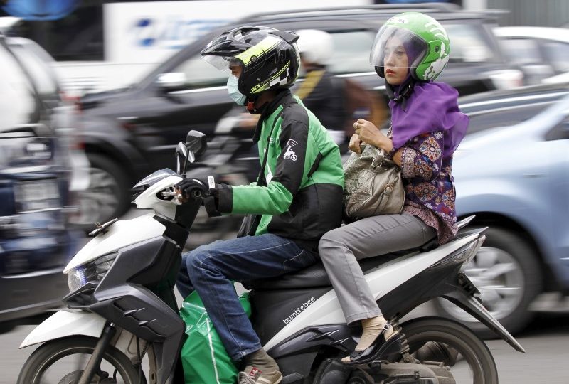 A woman rides on the back of a motorbike, part of the Go-Jek ride-hailing service, on a busy street in central Jakarta, Indonesia December 18, 2015. REUTERS/Garry Lotulung
