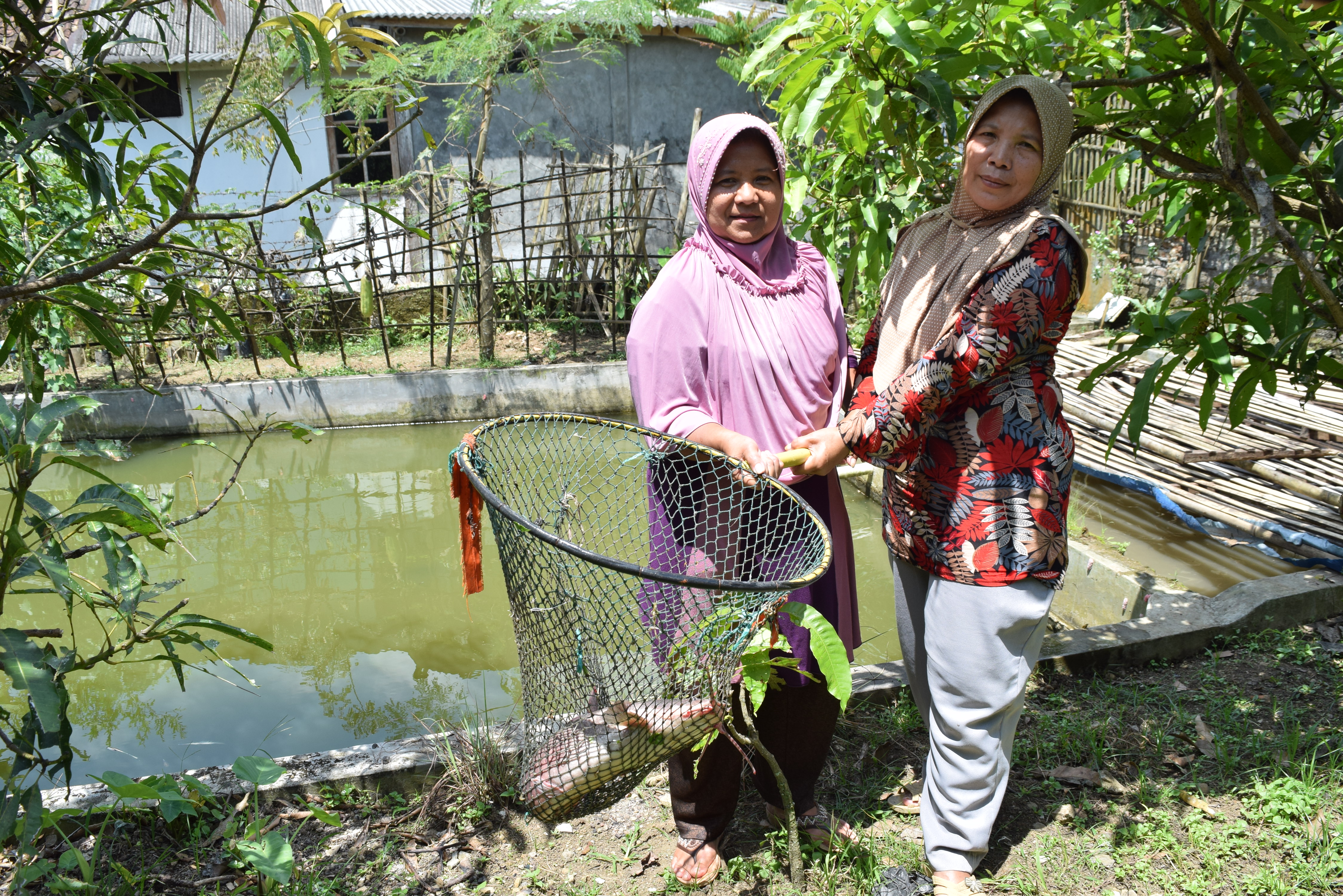 Indonesian former domestic helpers Enok Salamah (left) and Aan (right) hold a catfish in a net at a fish farm in Caringin village on Indonesia’s Java island on April 10, 2017. The catfish farm is an initiative to help victims of trafficking to reintegrate into society. Thomson Reuters Foundation/Beh Lih Yi