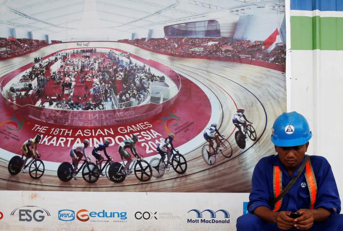 A worker sit near a banner of 2018 Asian Games during renovation of velodrome for 2018 Asian Games in Jakarta, Indonesia, March 6, 2017. REUTERS/Beawiharta