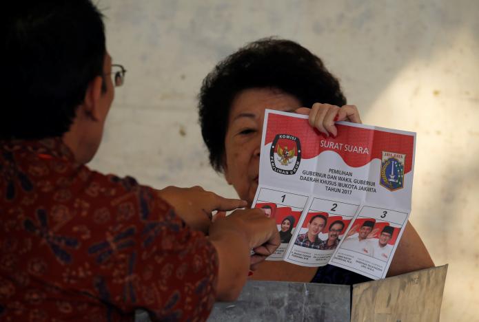 An election official assists an ethnic Chinese Indonesian woman before she casts her ballot during an election for Jakarta’s governor, in Jakarta, Indonesia, February 15, 2017. REUTERS/Beawiharta
