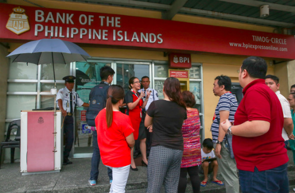 A bank officer talks to customers waiting to get inside the Bank of the Philippine Islands branch on Panay Avenue in Quezon City on Wednesday. The bank said a system glitch affected their computer system resulting in unauthorized transactions in various accounts. Fernando G. Sepe Jr., ABS-CBN News
