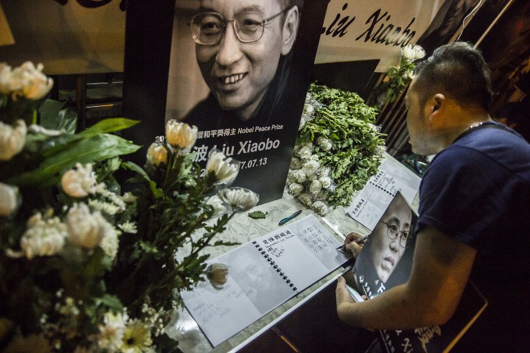 A man writes a message and holds a portrait outside the Chinese Liaison Office of Hong Kong after the death of Chinese Noble laureate Liu Xiaobo, in Hong Kong on July 13, 2017. AFP PHOTO / Isaac Lawrence