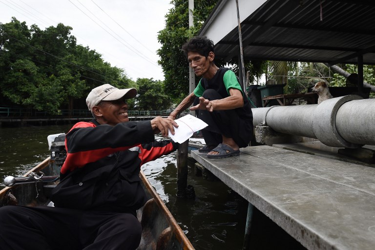 This photo taken on July 17, 2017 shows postman Nopadol Choihirun (L) delivering mail to a resident in the Bang Khun Thian district on the outskirts of Bangkok. Photo: Lillian Suwanrumpha/ AFP