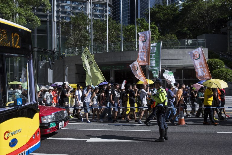 A police officer (centre R) stops traffic as protesters march in Hong Kong on August 20, 2017, to protest the jailing of Joshua Wong, Nathan Law and Alex Chow (not pictured), the leaders of Hong Kong’s ‘Umbrella Movement’, after their sentencing at the High Court on August 17. 
Wong, Law and Chow were handed sentences of six to eight months by the Court of Appeal for their role in 2014’s massive Umbrella Movement protests, which called for fully free leadership elections and were an unprecedented challenge to Beijing. / AFP PHOTO / ISAAC LAWRENCE