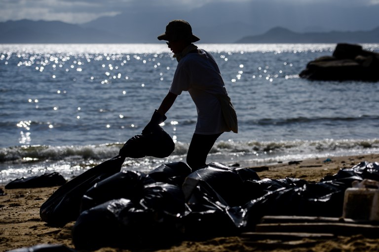 A volunteer drags a black bin bag as she helps remove washed up palm oil from a beach on Hong Kong’s outlying Lamma Island on August 8, 2017. 
AFP PHOTO / ANTHONY WALLACE