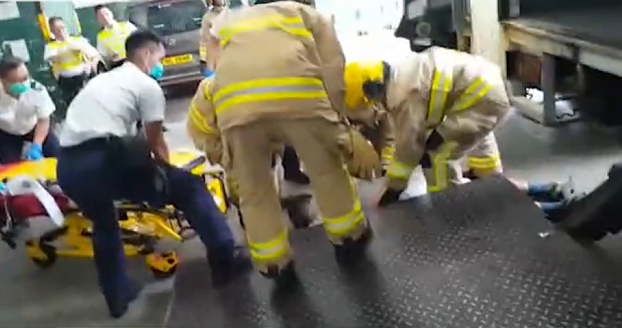 Firefighters tend to a driver pulled from between trucks in Kowloon Bay. Screenshot: Apple Daily