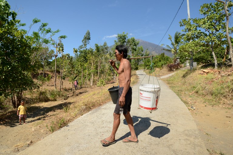 A villager carries buckets to take water behind seen mount Agung at Kubu subdistrict in Karangasem on Bali island on October 6, 2017. Photo: Sonny Tumbelaka/AFP