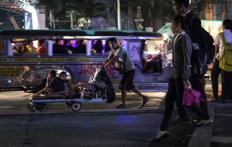 A father pushes a wooden cart with his children along a street in Manila on November 24, 2017. AFP PHOTO / Noel Celis
