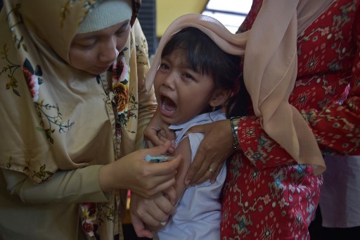 An Indonesian girl cries as she receives a vaccination shot against diphtheria at a village clinic in Jakarta on December 11, 2017. AFP PHOTO / ADEK BERRY