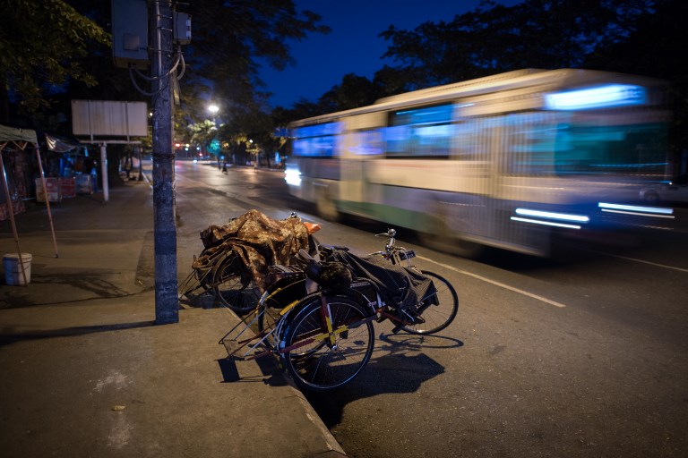 This photo taken on December 3, 2017 shows trishaw drivers sleeping on top of their cycles as an early morning bus rushes by in Yangon. / AFP PHOTO / Roberto SCHMIDT
