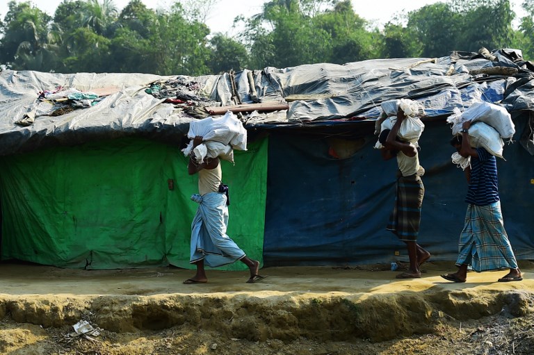 Rohingya refugees carry relief material next to a settlement near the ‘no man’s land’ area between Myanmar and Bangladesh in Tombru in Bangladesh’s Bandarban on February 27, 2018. / AFP PHOTO / MUNIR UZ ZAMAN