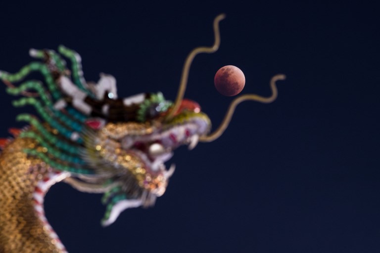 The moon rises over the horizon above the head of a Chinese dragon statue in Bangkok, Jan. 31, 2018. Photo: Roberto Schmidt/ AFP