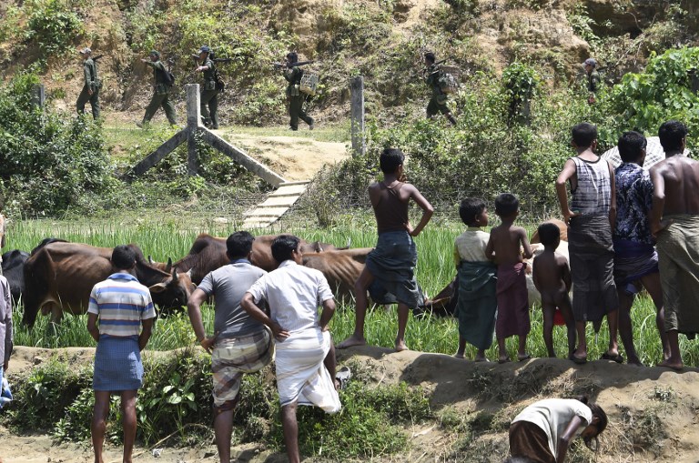 In this photograph taken on September 16, 2017, Rohingya Muslim refugees in Jalpatoli refugee camp, in the no-man’s land area between Myanmar and Bangladesh, watch as Myanmar soldiers patrol on the other side of the border. / AFP PHOTO / DOMINIQUE FAGET / XGTY