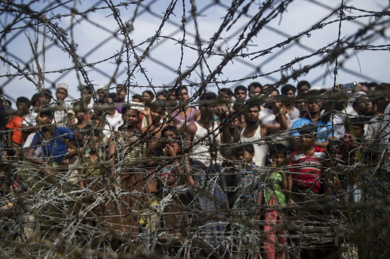 This picture taken from Maungdaw district, Myanmar’s Rakhine state on April 25, 2018 shows Rohingya refugees gathering behind a barbed-wire fence in a temporary settlement setup in a “no man’s land” border zone between Myanmar and Bangladesh. / AFP PHOTO / Ye Aung THU
