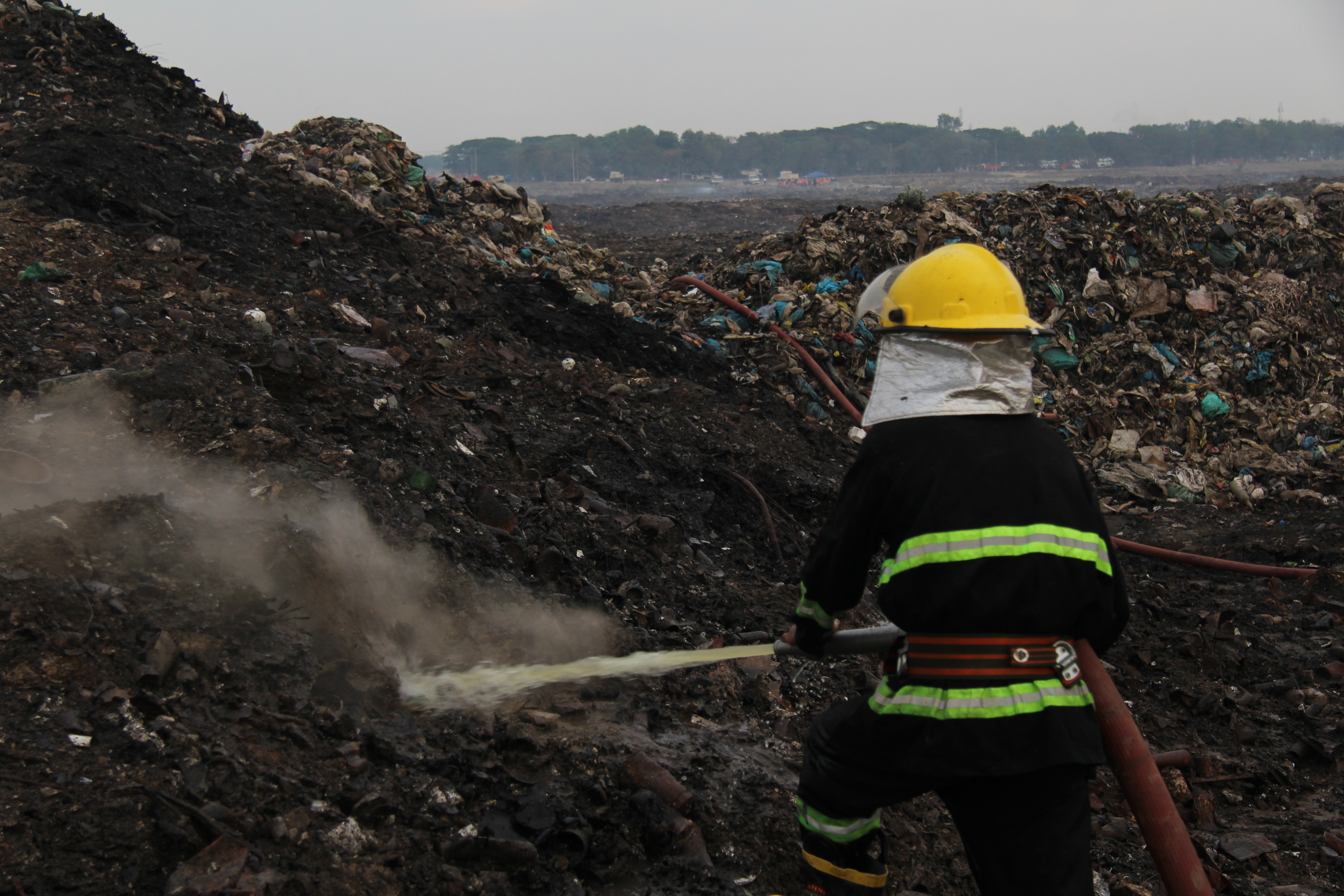 A firefighter sprays water at a plume of smoke rising from the ground inside the Htein Bin landfill on May 3, 2018.