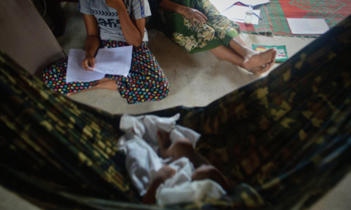 The baby of undocumented Burmese Muslim parents naps in a hammock while relatives sit nearby. Photo: BHRN