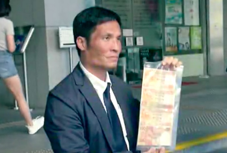 Man holds up the counterfeit money used as props for an award-winning Hong Kong gang film. screengrab via Apple Daily video.