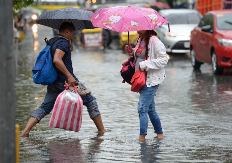 People cross a flooded street in Manila on July 17, 2018, as a tropical depression, locally named Henry, made landfall in northern Luzon island affecting suburban Manila and nearby provinces with monsoon rains, according to weather bureau report.(Photo: Ted Aljibe, AFP)