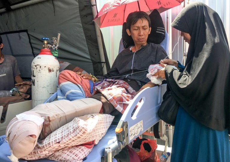 This picture taken on August 6, 2018 shows quake survivor Alimuddin (L) sitting with his wife Maria Ulfa (R) in a hospital bed at a makeshift ward outside the local hospital in Mataram on Lombok island, after the area was struck by an earthquake the night before. Photo: Kiki Siregar/AFP