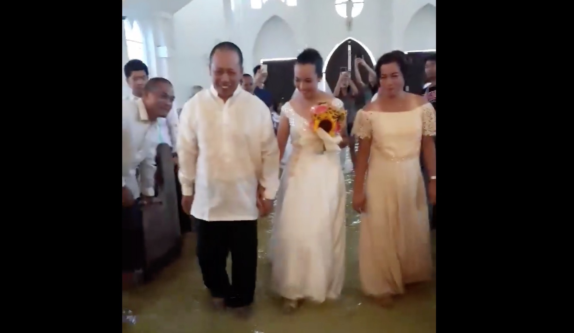 Bride Jobel Delos Angeles walks down the flooded aisle with her parents on her wedding day. 