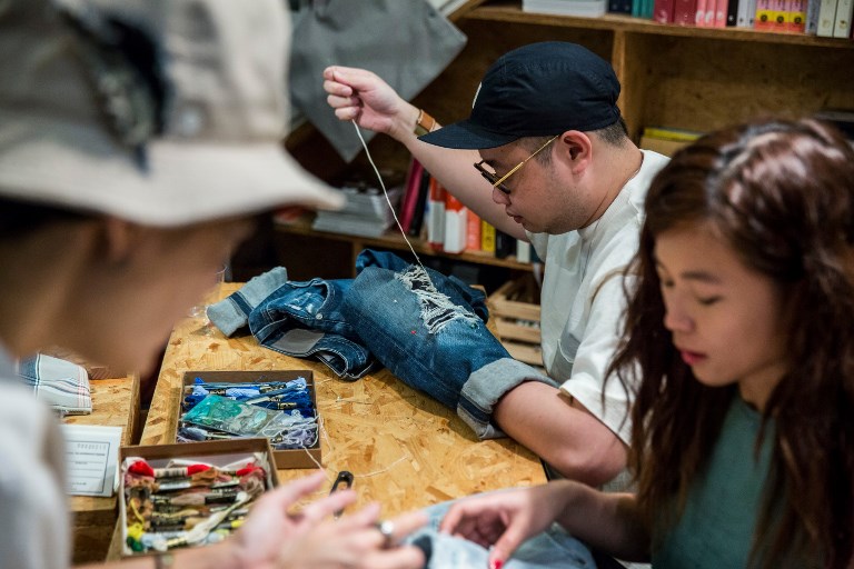 This picture taken on September 9, 2018 shows a participant at a “Fashion Clinic” workshop mending his old jeans. 
Despite Hong Kong’s reputation for rampant consumerism, a nascent movement against fast fashion is taking root in the city, with clothes-mending workshops and pop-up swaps growing in popularity, and designers parading recycled fabrics on the catwalk. / AFP PHOTO / Isaac LAWRENCE / TO GO WITH HongKong-fashion-environment-textile-lifestyle, FEATURE by Yan ZHAO