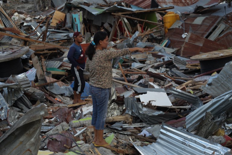 In this photo taken on October 6, 2018, Nonlis Kando (R), 35, stands among debris in Petobo, Indonesia’s Central Sulawesi, following the September 28 earthquake and tsunami. 
Stepping gingerly through the pulverised remnants of her Indonesian village, Nonlis Kando spotted a white shoebox imprinted with neon red lips sticking up from the ruins, and burst into tears. / AFP PHOTO / YUSUF WAHIL