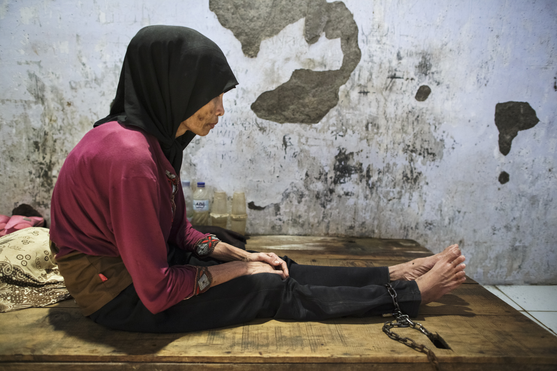 A young woman with a real or perceived psychosocial disability sits with her ankle chained to a platform bed at Bina Lestari faith healing center in Brebes, Central Java. Photo: Andrea Star Reese for Human Rights Watch