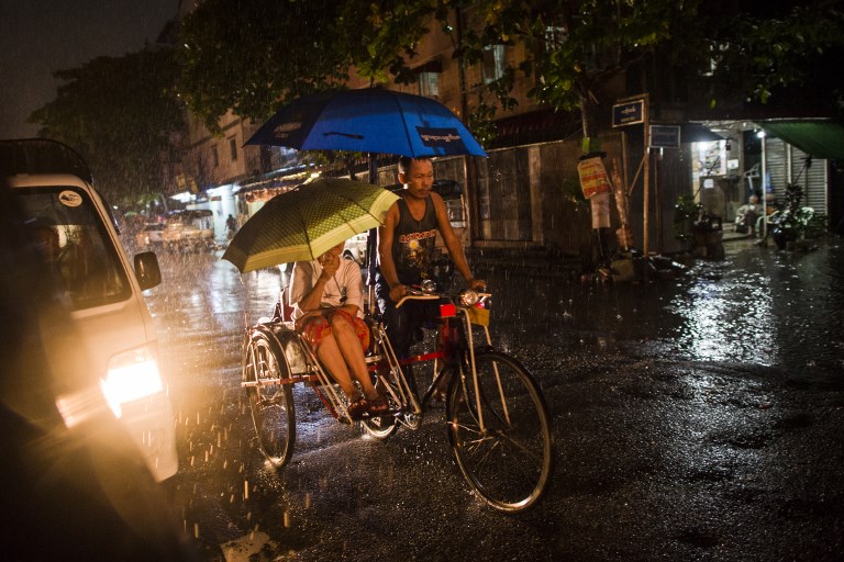 A man transports a woman on a tri-shaw along a road during monsoon rain in Yangon on August 2, 2018. – Monsoon rains have pummelled the Mekong region in recent days with Myanmar bearing the brunt of flooding that has forced 150,000 to flee and threatens to destroy levees shielding thousands of homes. (Photo by YE AUNG THU / AFP)