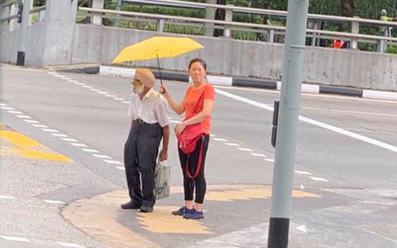 A Chinese lady is seen holding an umbrella for a Sikh uncle at a junction (Photo: Jonathan Vendi / Facebook)