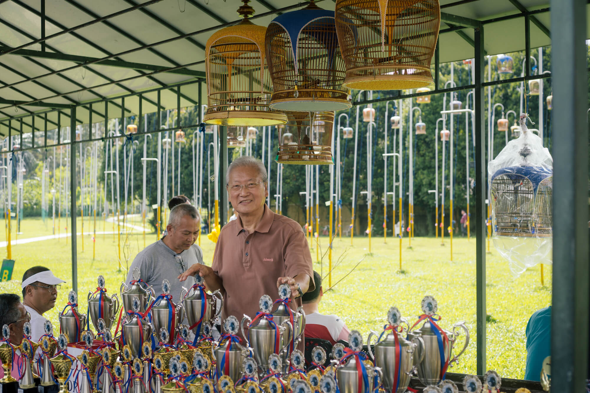 Robin Chua, standing behind the table of trophies. Photo: Christopher Sim / Coconuts Media