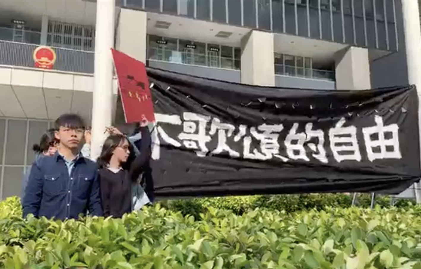 Pro-democracy activists Joshua Wong (left) and Agnes Chow (right) protest the national anthem law at Civic Square outside the Central Government offices. Screengrab  via Facebook video/Demosistō.