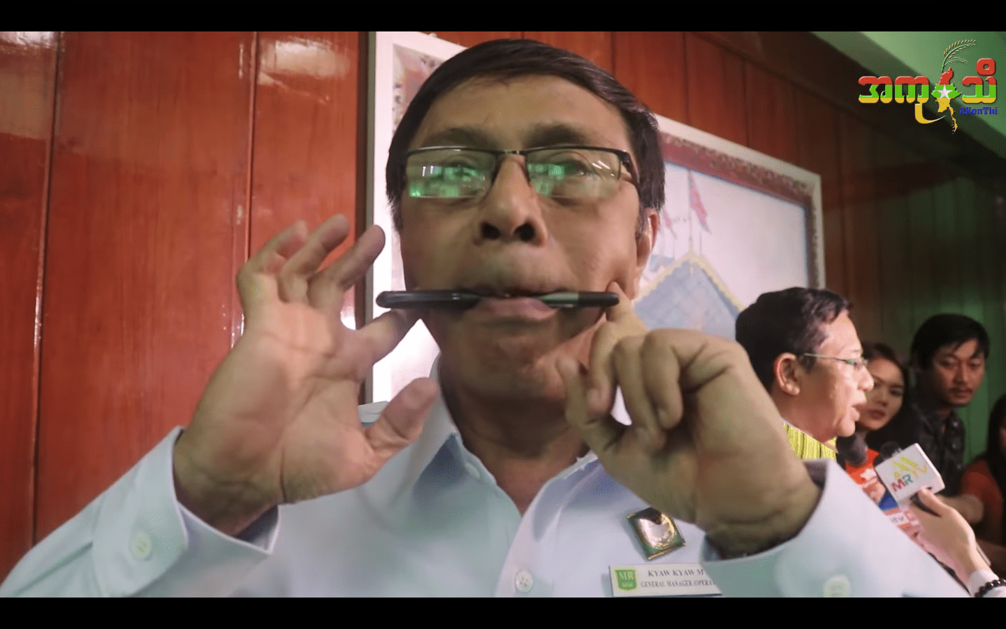Myanmar Railways General Manager U Kyaw Kyaw Moe demonstrating how to smile with a pen – screengrab via Akonthi video
