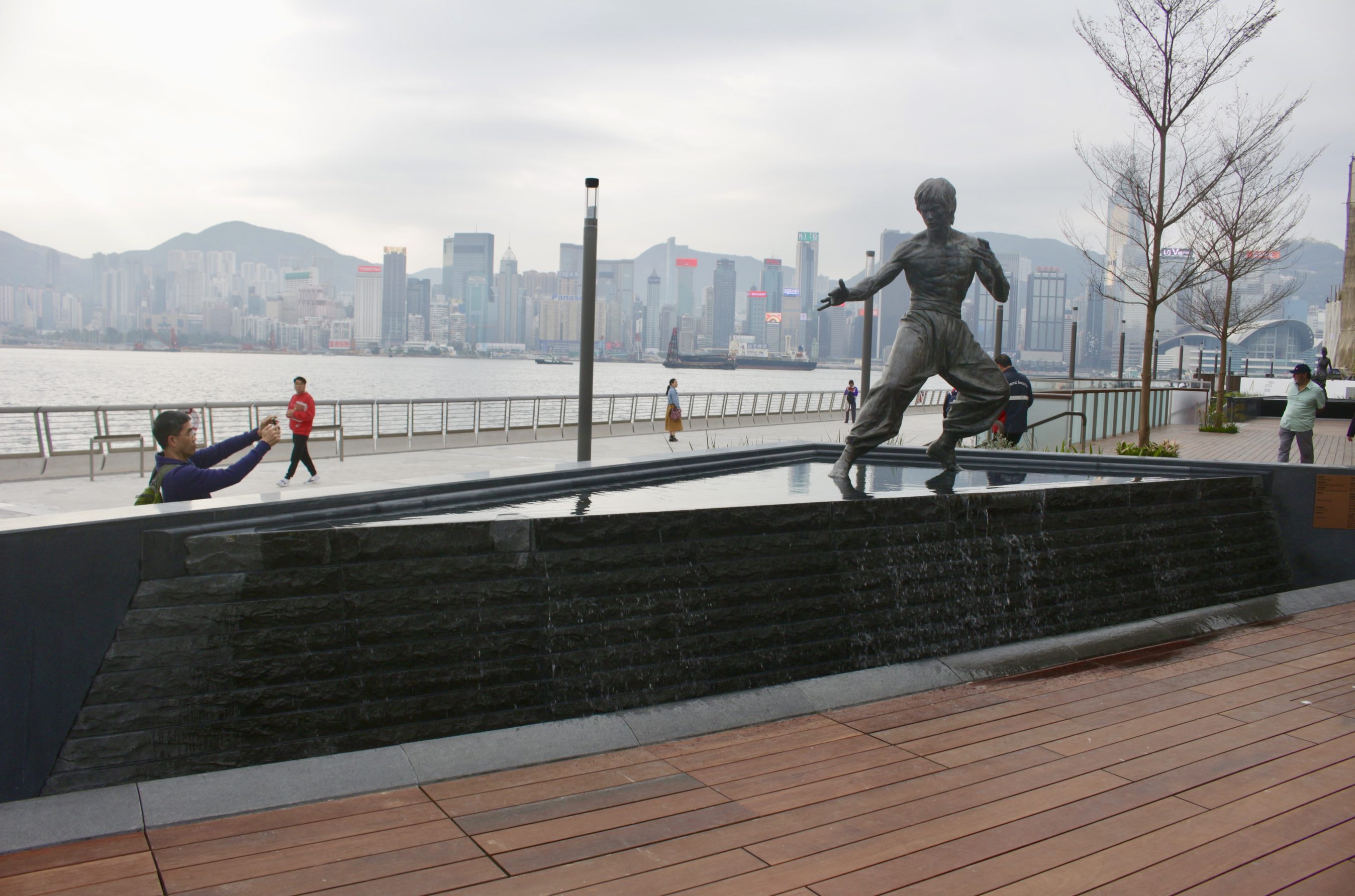 Bronze statue of kung fu movie legend Bruce Lee. His statue was previously surrounded by metal barrier to prevent people from touching the statue. Those barriers have now been replaced by a water feature with and is placed with Victoria Harbour in the background. Photo by Vicky Wong.