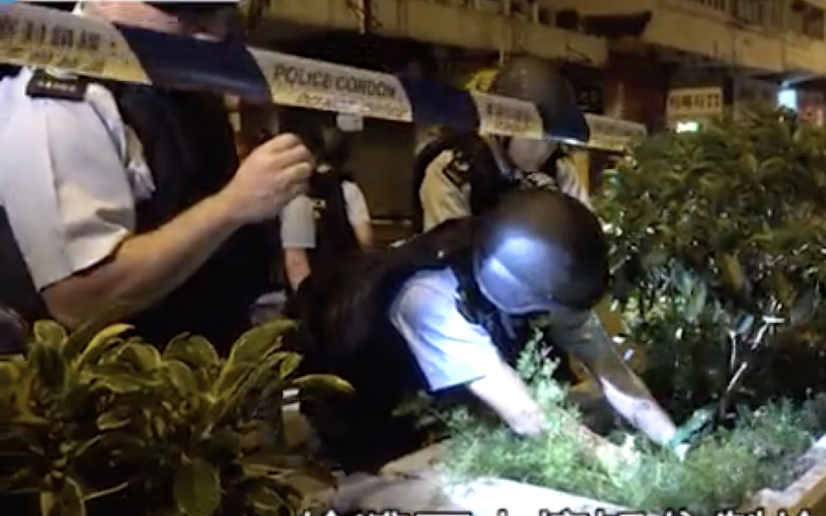 Police looking through the bushes for evidence near the scene of a shooting in Sham Shui Po. Screengrab via Apple Daily video.