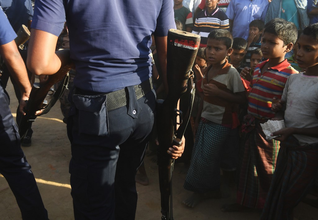 (FILES) In this file photo taken on November 15, 2018, Rohingya refugees look on as Bangladeshi police officers walk past at the Unchiprang refugee camp near Teknaf. – Criminal gangs and militants are increasing their grip on Rohingya refugee camps in Bangladesh committing killings and abductions with “impunity”, International Crisis Group said April 25. Photo by Dibyangshu Sarkar / AFP