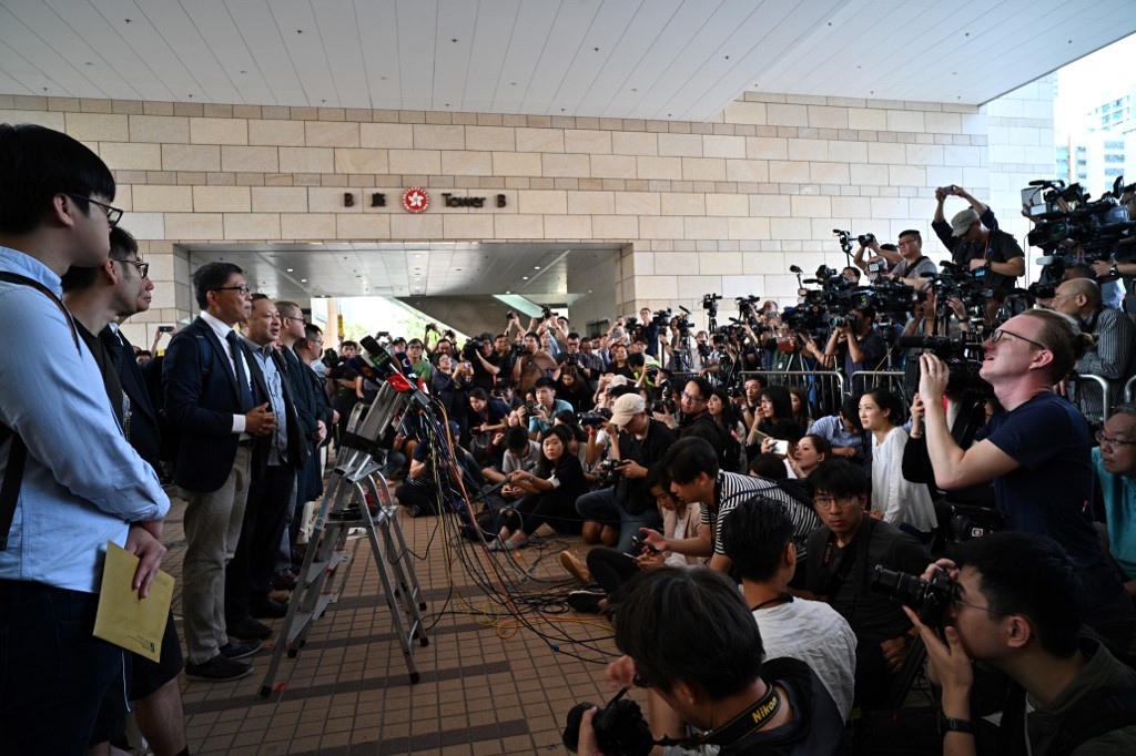 Sociology professor Chan Kin-man (third left, white shirt), law professor Benny Tai (fourth left), and other pro-democracy campaigners speak to the press outside the West Kowloon Magistrates Court today. Photo via AFP.