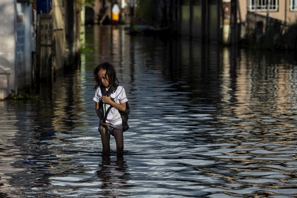 This photo taken on October 8, 2018 shows an elementary student wading through floodwaters in Mabalacat, Pampanga. – Areas north of Manila like the provinces of Pampanga and Bulacan have sunk four-six centimetres (1.5-2.4 inches) a year since 2003, according to satellite monitoring. Photo by Noel Celis/AFP 