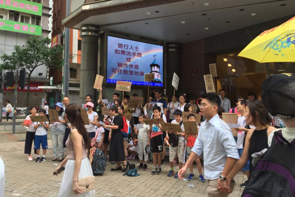 A group of schoolchildren sing protest songs from the 2014 Umbrella Movement on the sidelines of the anti-extradition protest today. Photo by Stuart White.