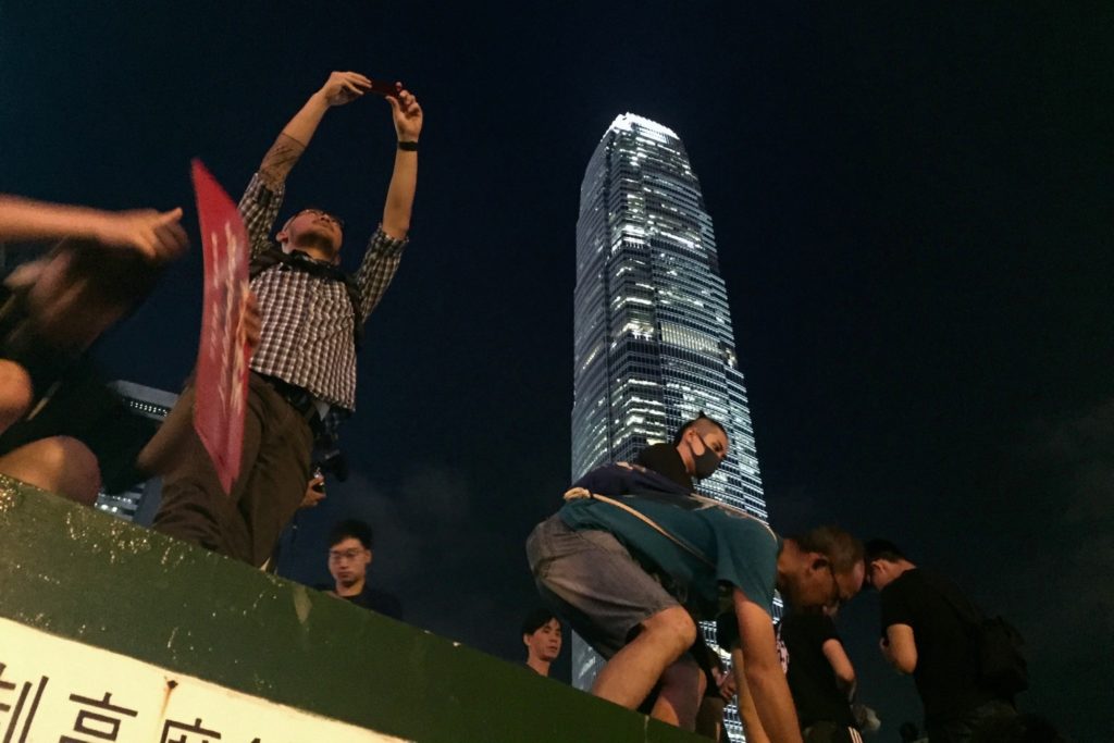 Protesters hoist others onto the roof of a structure on top of a nearby parking garage to watch tonight's rally. Photo by Stuart White.