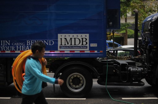 A worker walks past a poster of the 1 Malaysia Development Berhad (1MDB) logo on a truck in Kuala Lumpur on March 14, 2016. (Photo by MOHD RASFAN / AFP)