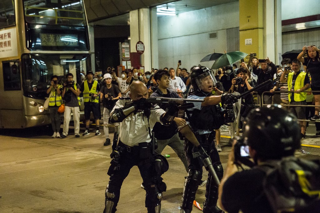 A police officer points a firearm during clashes with protesters who had gathered outside Kwai Chung police station. Photo via AFP.
