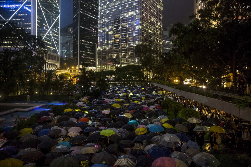 People from the finance community hold up umbrellas and shine lights during a protest in Central last night. Photo via AFP.