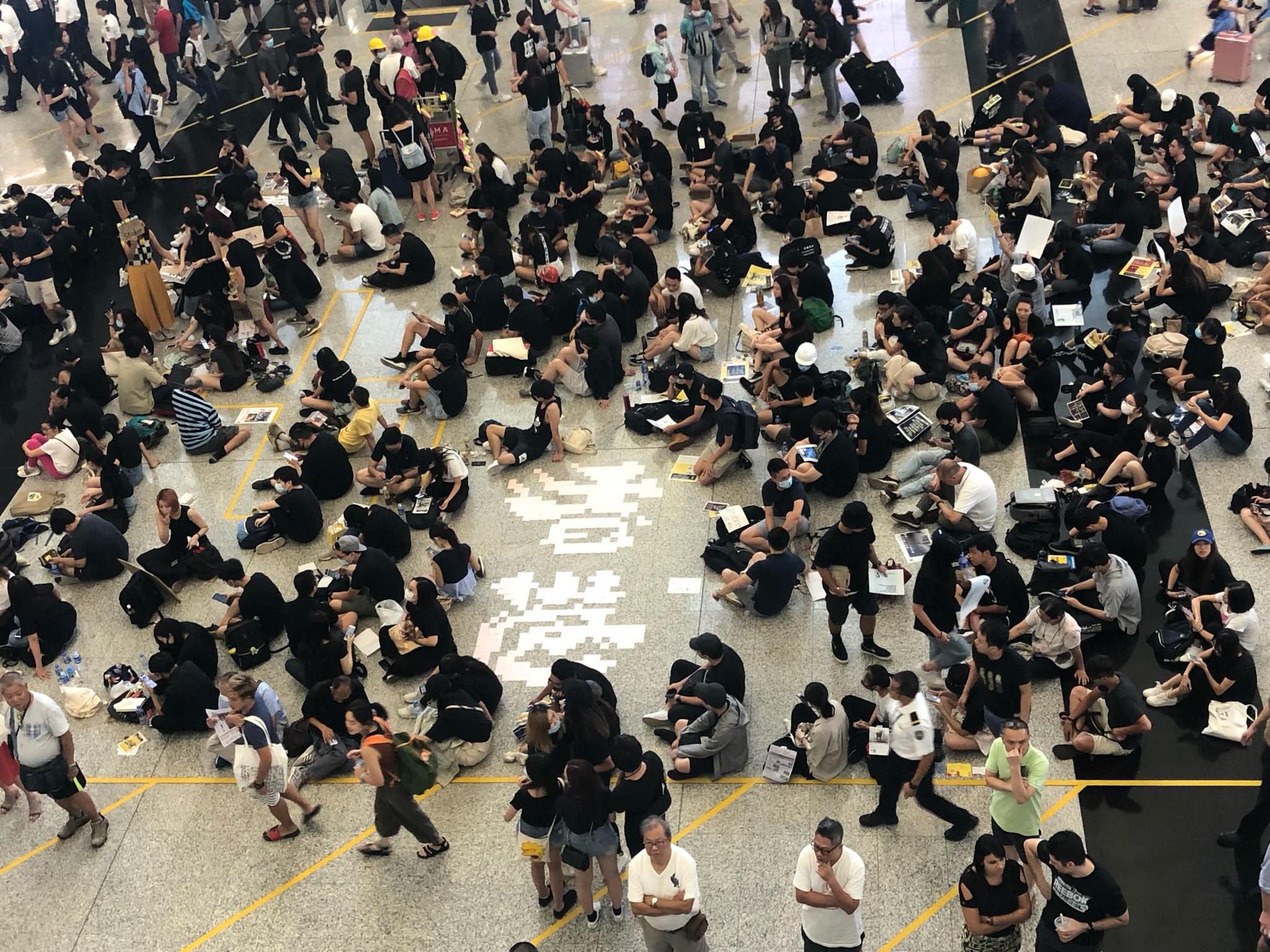 Protesters sit on the floor of Hong Kong International Airport today, surrounding a display with the characters for “Hong Kong” fashioned out of Post-It notes. Photo by Iris To.