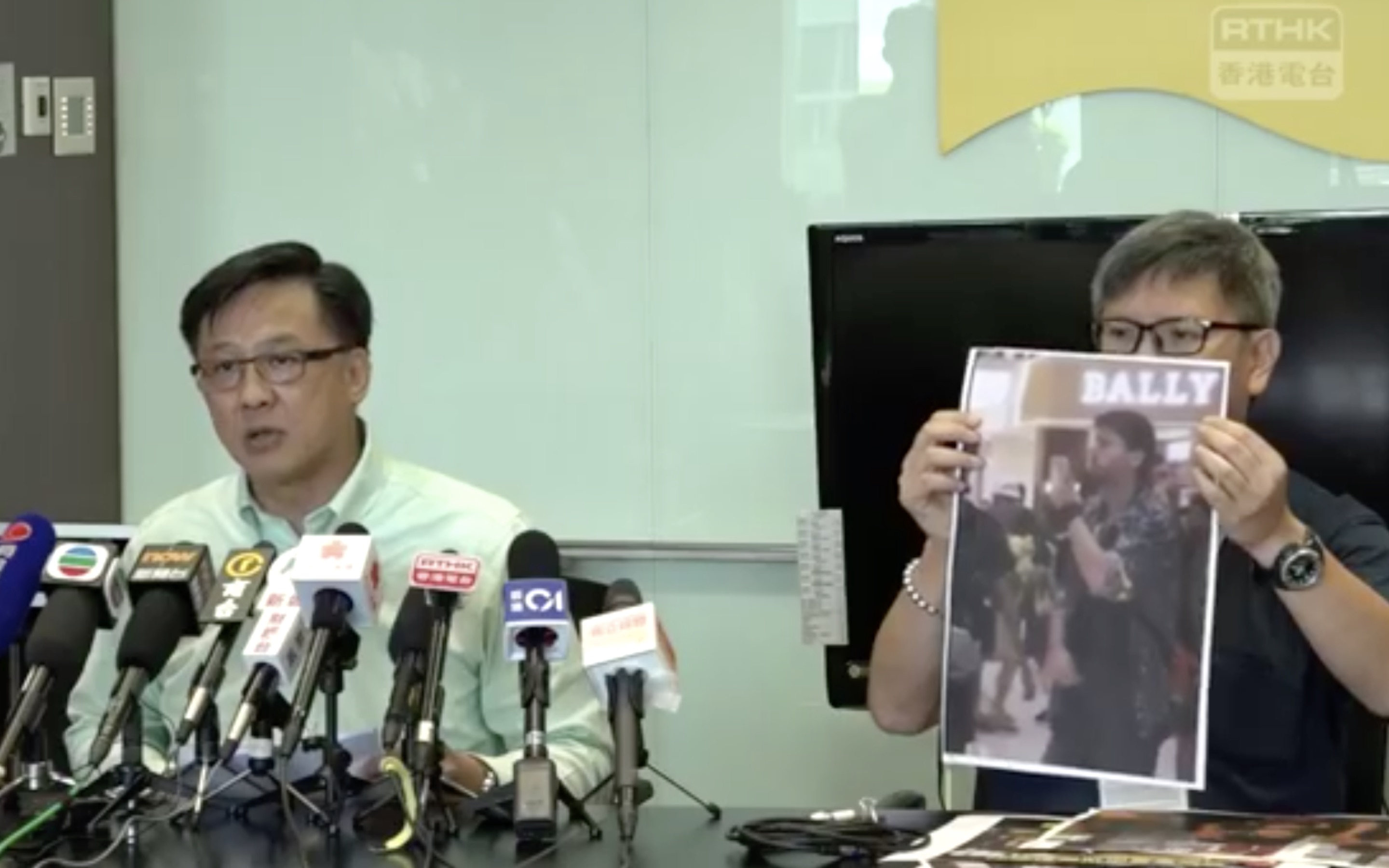 Junius Ho’s aide holds up a photo of a man they claim is a foreign commander responsible for stoking recent protests. Screengrab via Facebook/RTHK.