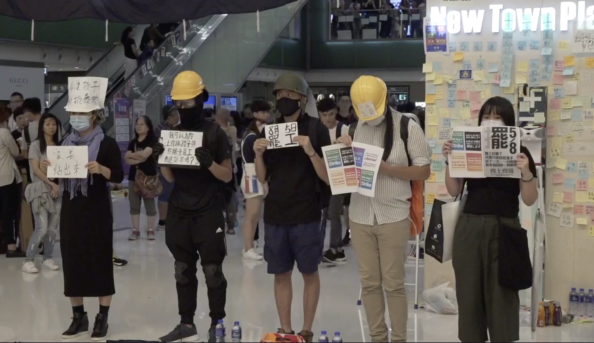 Protesters at New Town Plaza in Sha Tin last night hold up signs calling on Hongkongers to support a citywide strike on Monday. Screengrab via Facebook/Stand News.