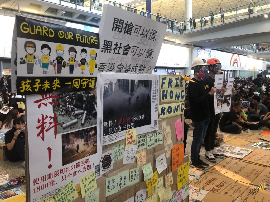 Protesters stand next to a display featuring information about the recent unrest at the Hong Kong International Airport today. Photo by Iris To.