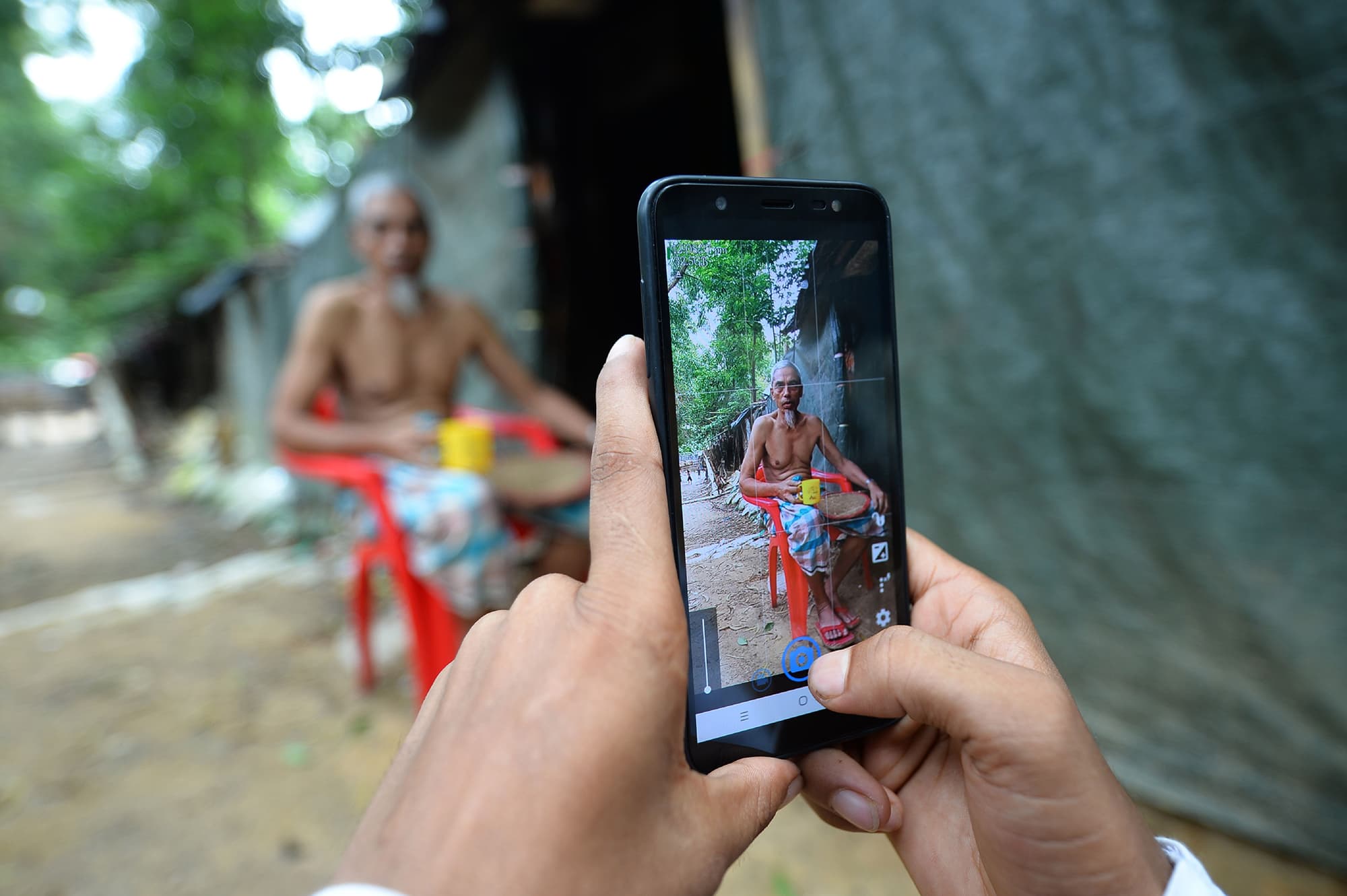 In this picture taken on July 23, 2019, Rohingya youth Mohammad Rafiq uses his mobile phone to take photos of a man by his shack at the Kutupalong refugee camp.  Photo by Munir Uz Zaman/AFP