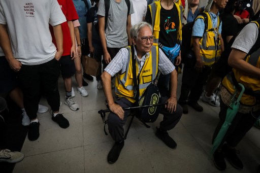 This picture taken on September 7, 2019 shows “Grandpa Wong” (C), 85, taking a rest on a portable stool set up in between a group of protesters in the Tung Chung district in Hong Kong. – Despite his age, Wong is a regular sight at Hong Kong’s street battles, hobbling towards police lines, placing himself in between riot officers and hardcore protesters, hoping to de-escalate what have now become near daily clashes. (Photo by VIVEK PRAKASH / AFP)